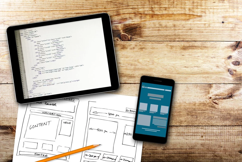 hand drawing of webpage wireframe, mockup on phone, webpage HTML code on tablet